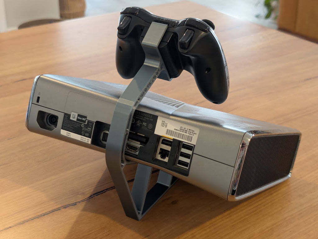 Silver Xbox 360 console and controller on a 3D printed display stand, rear view