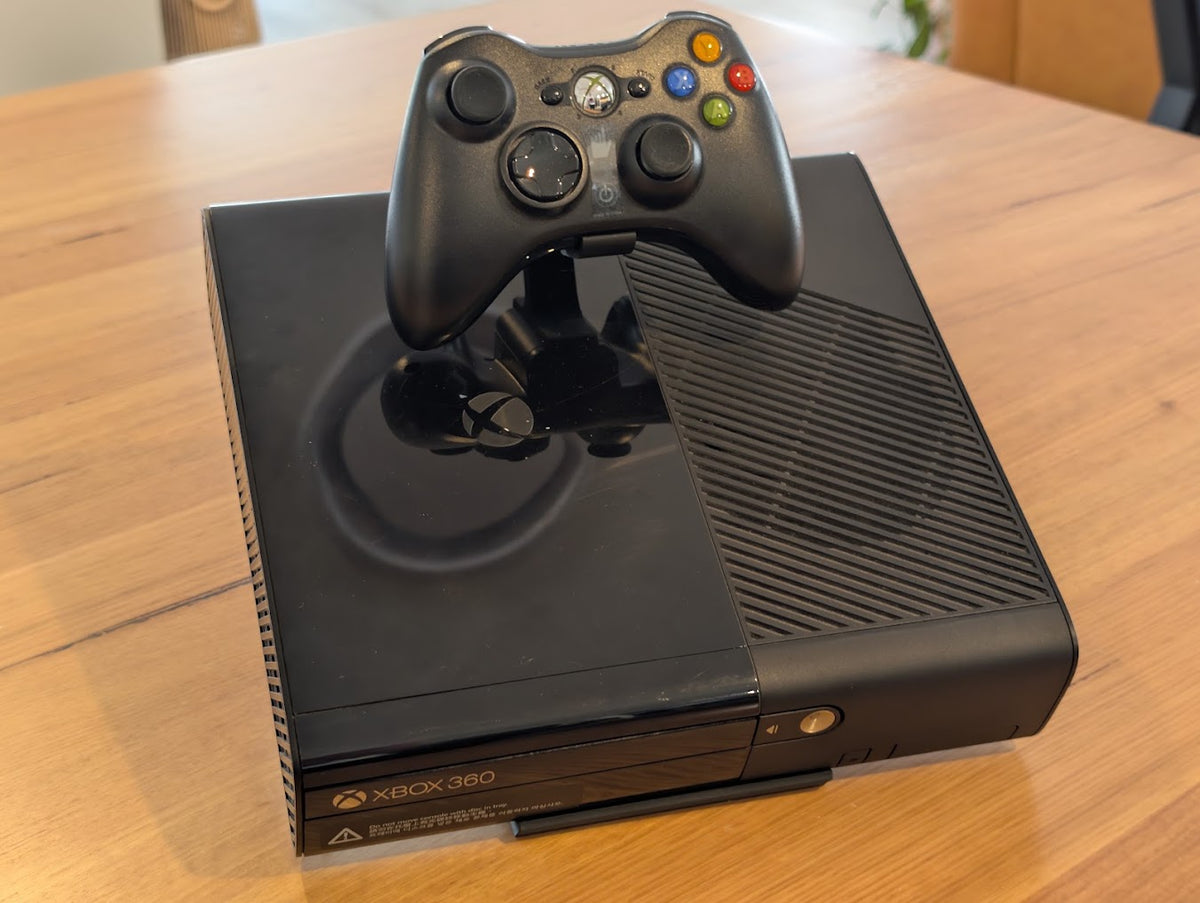 Black Xbox 360 console on a 3D printed display stand with a controller held above it