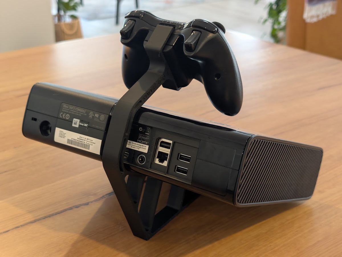 Xbox 360 console tilted on a 3D printed stand, rear view, with controller mount